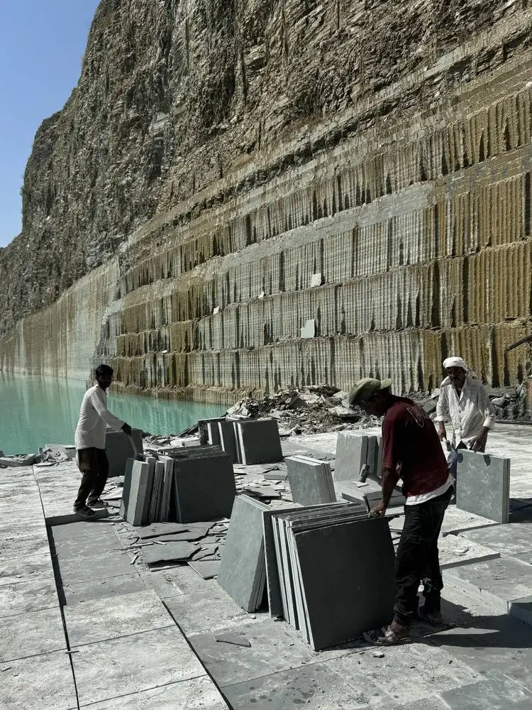 Workers sorting stacked slabs beside the water in the quarry pit