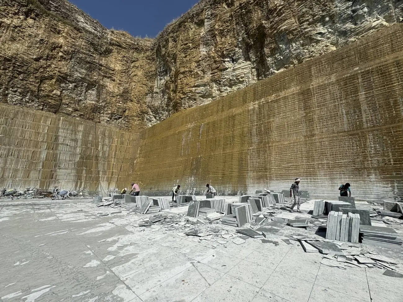 Workers sorting Kota stone slabs below the cut wall of the quarry